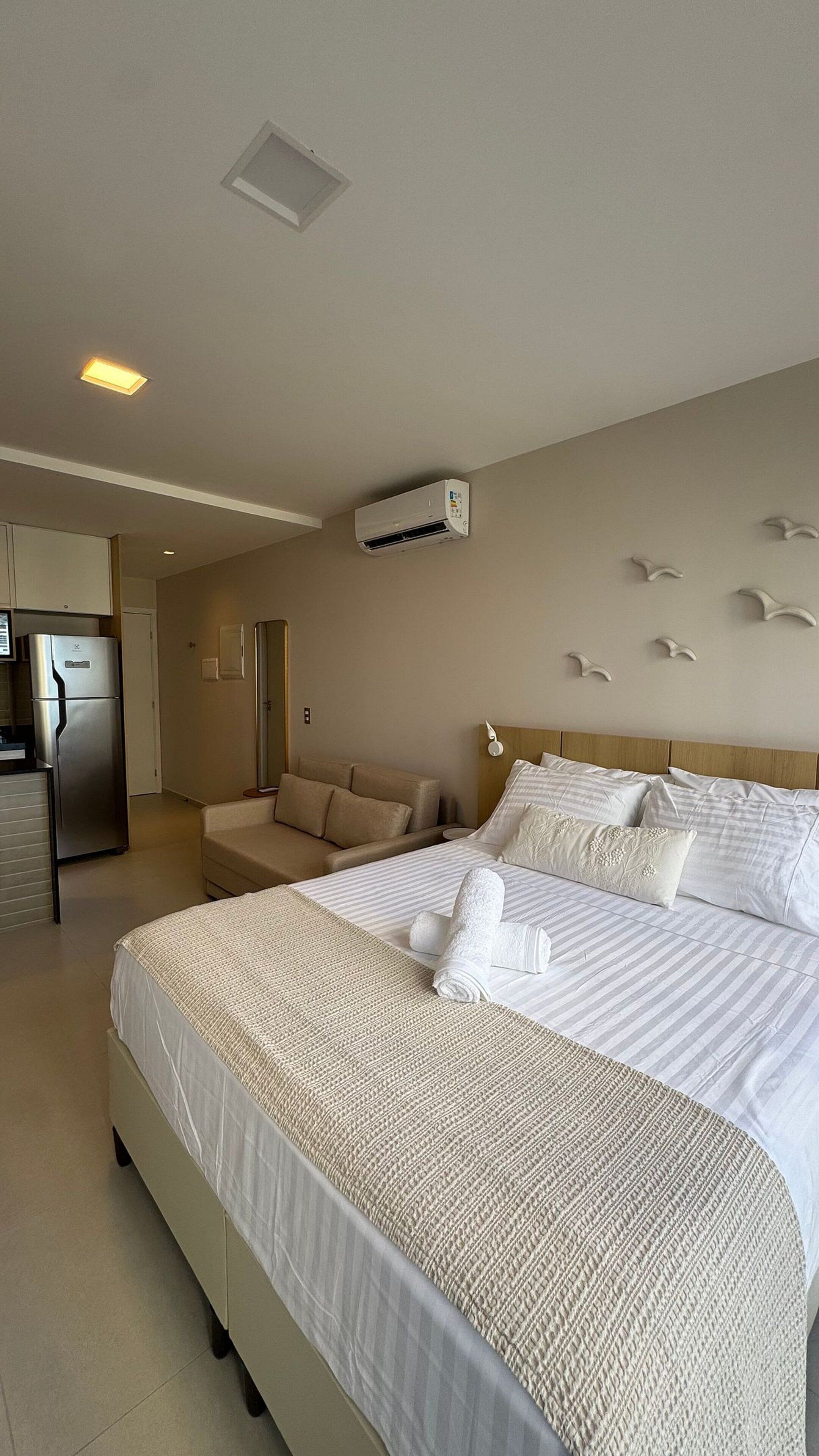 A hotel room with a large bed, a sofa, a kitchenette, and a bathroom.