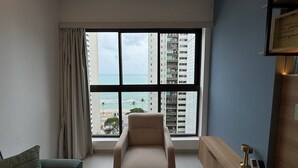 A room with a large window, a chair, a small table, and a framed picture on the wall.