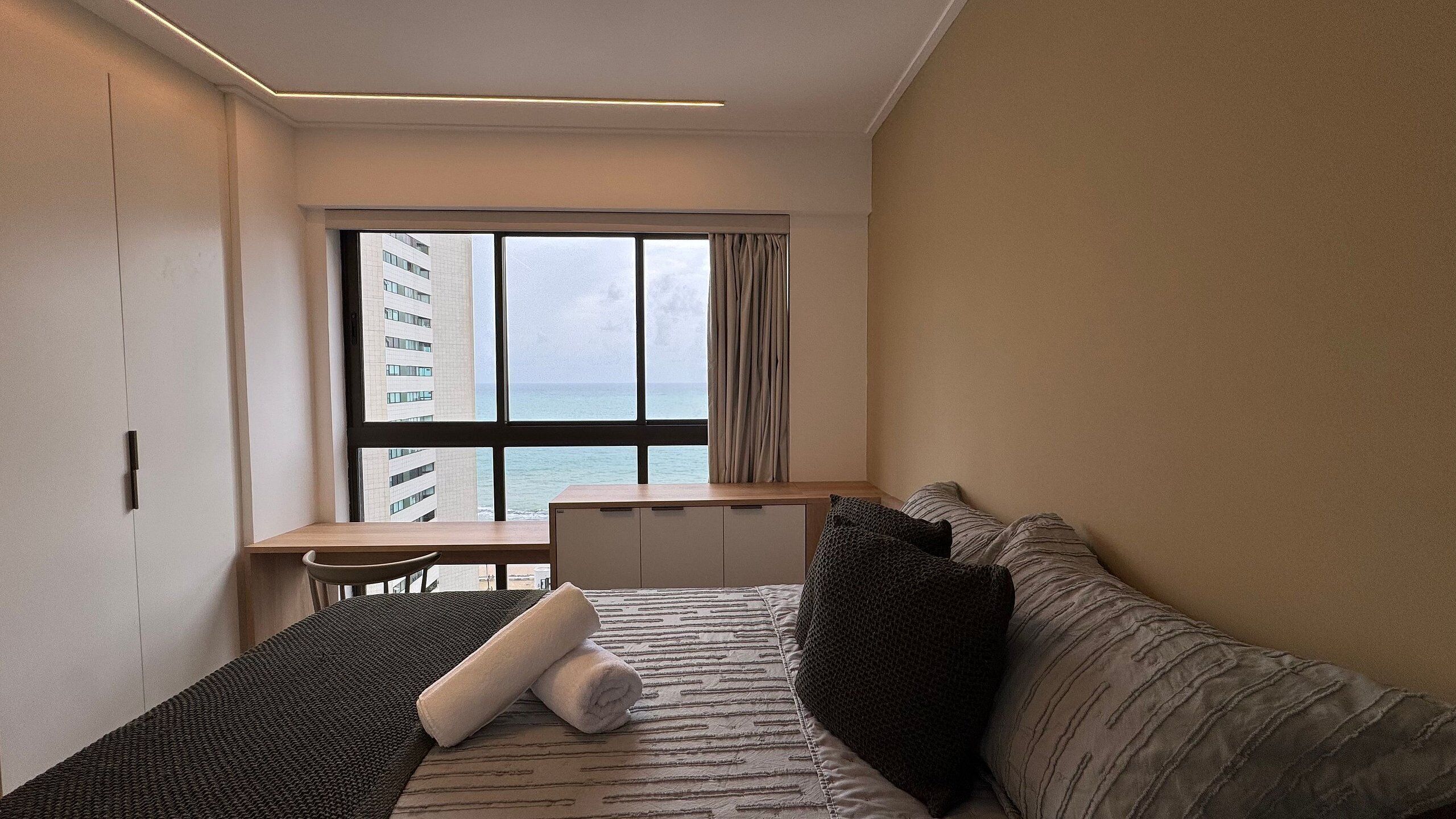 A hotel room with a bed, a desk, and a view of the sea.