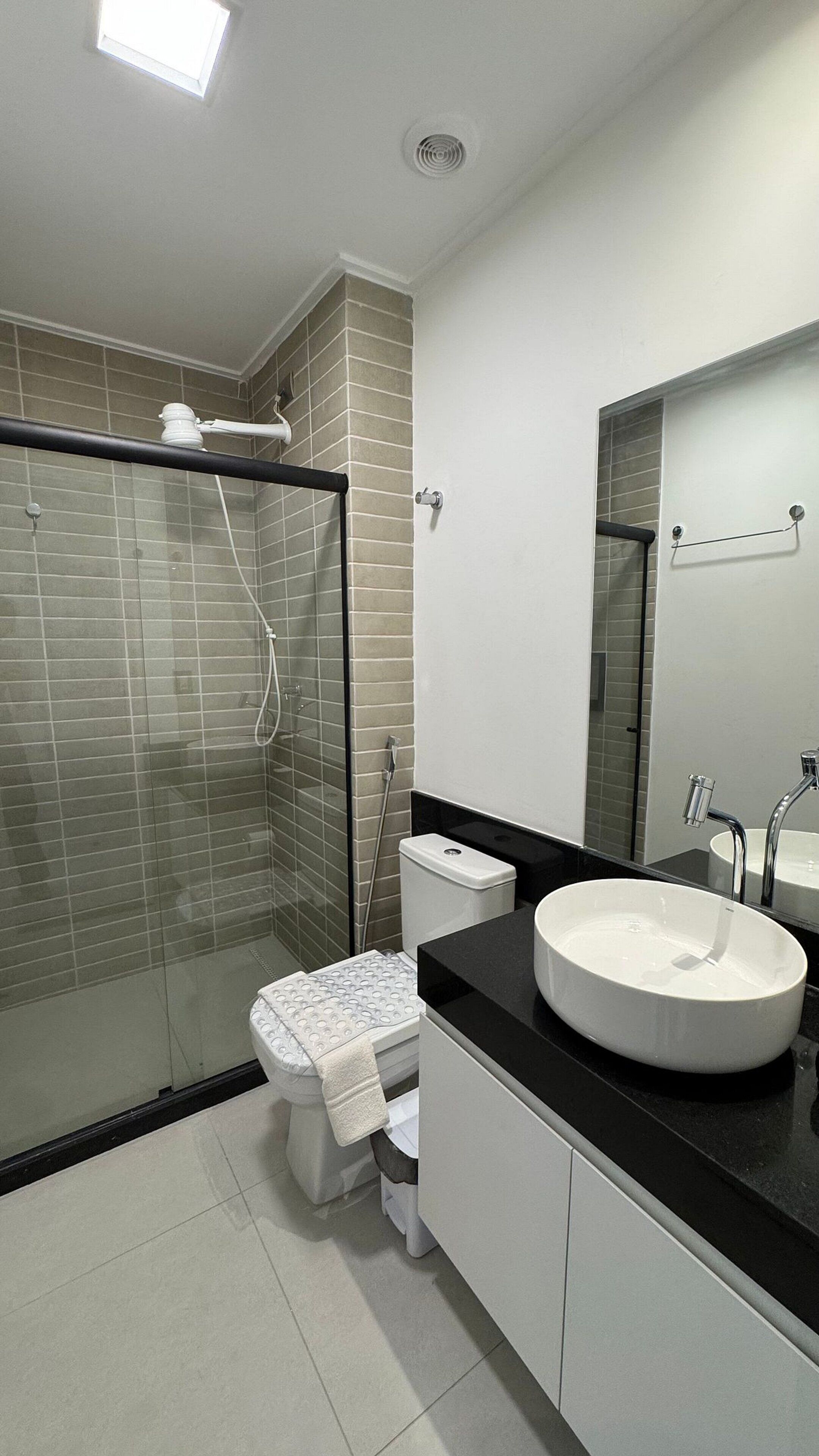 A modern bathroom with a glass-enclosed shower, a white toilet, and a black countertop with a white sink.