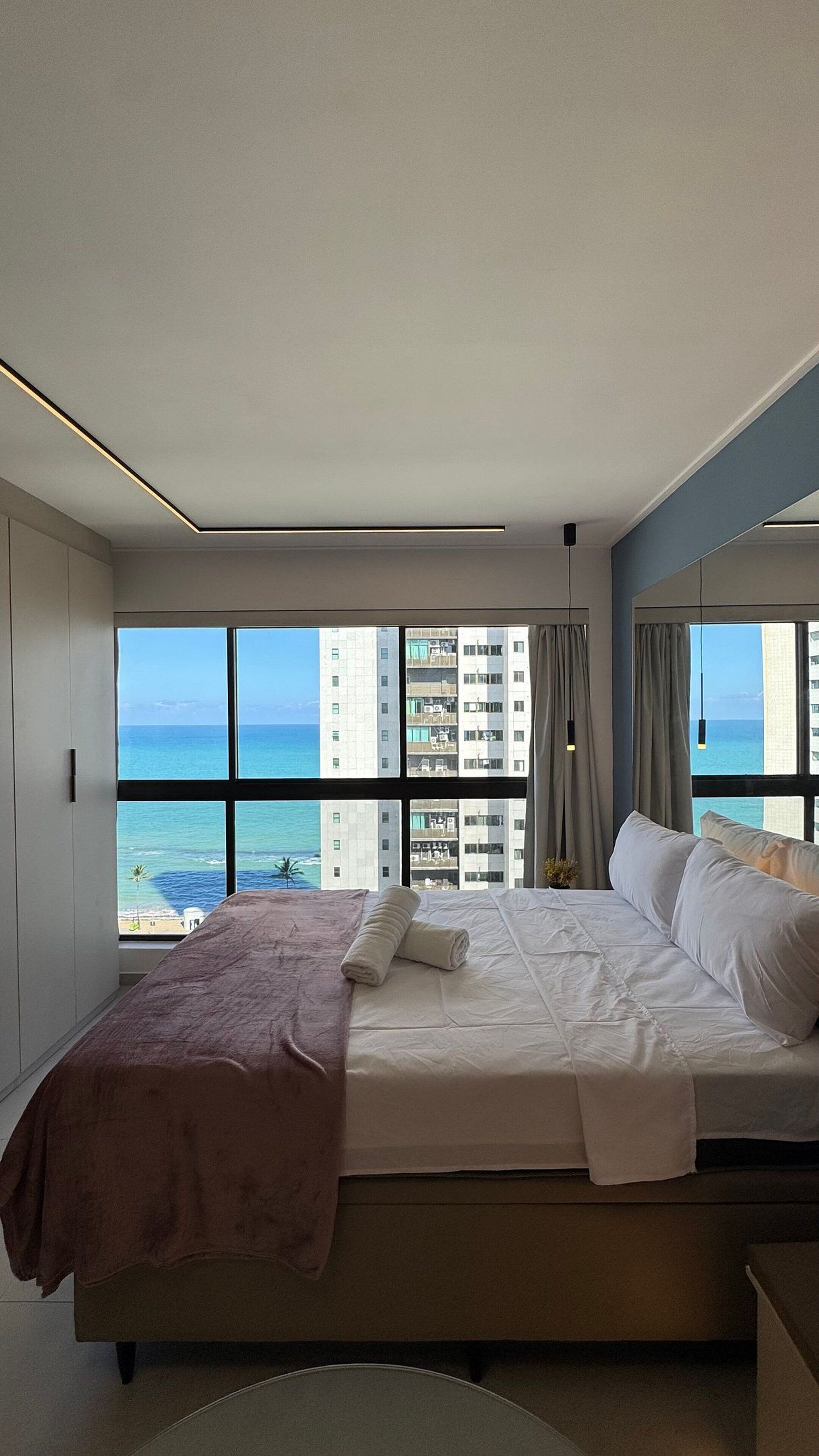 A hotel room with a bed, a view of the ocean, and a cityscape.