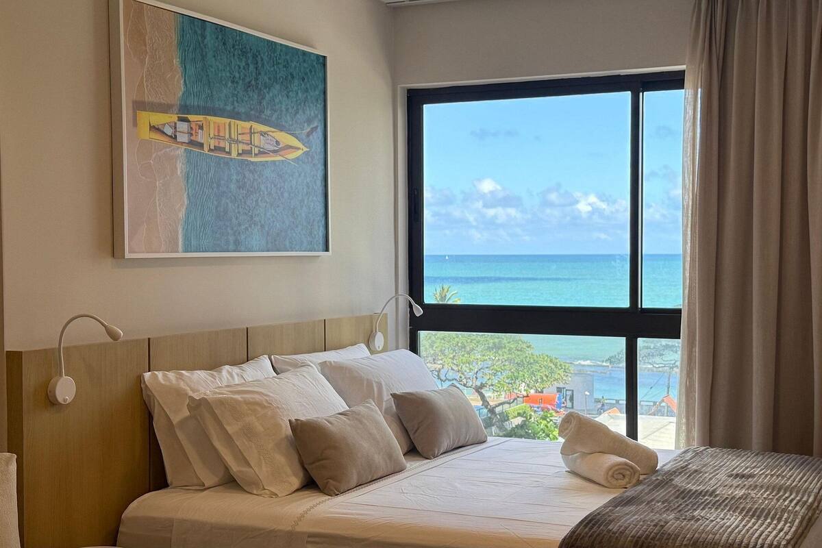Una habitación de hotel con una cama, una ventana que da al océano y un cuadro en la pared.