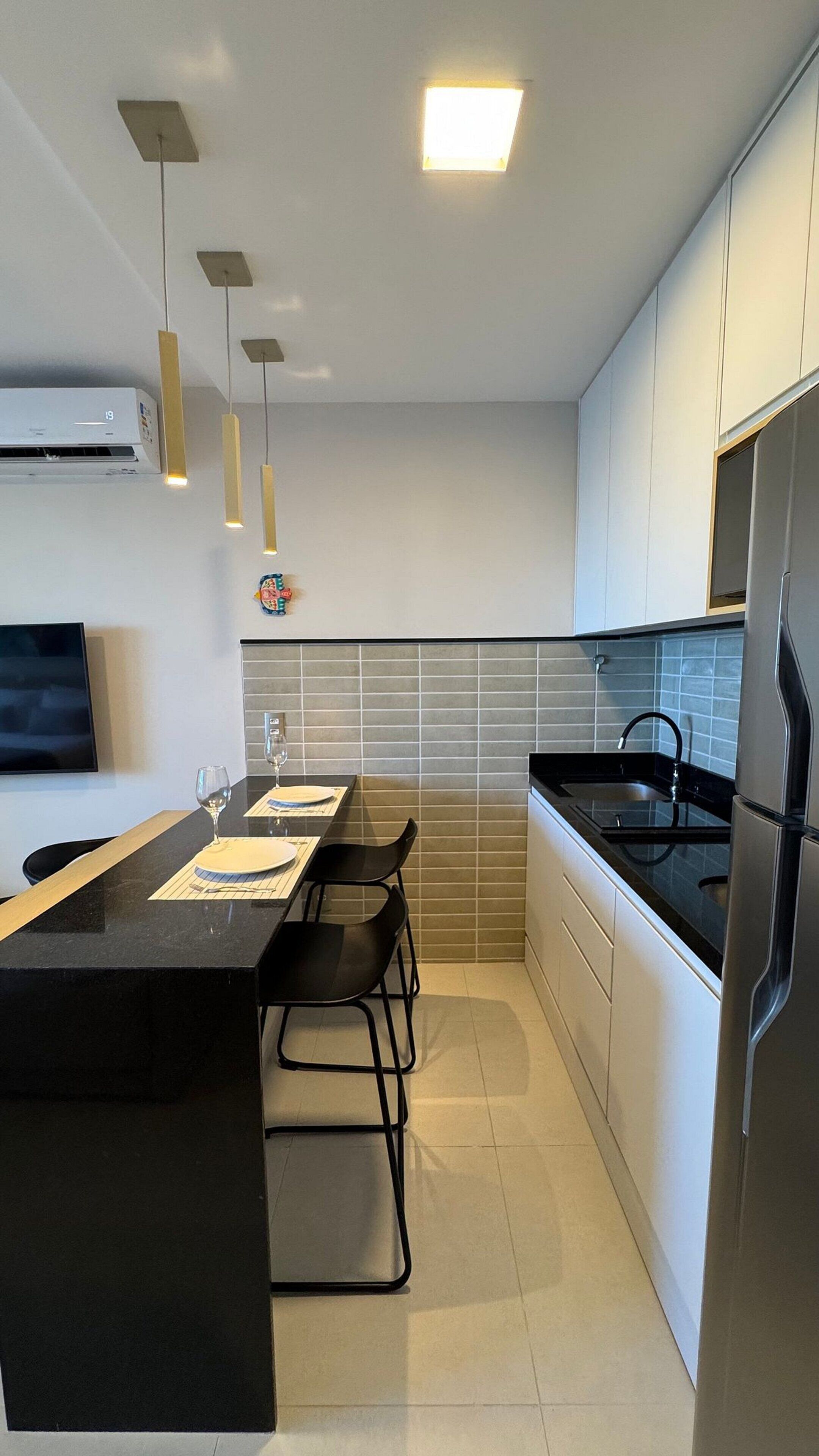 Uma cozinha moderna com ilha central, luminárias pendentes, fogão embutido e armários brancos.