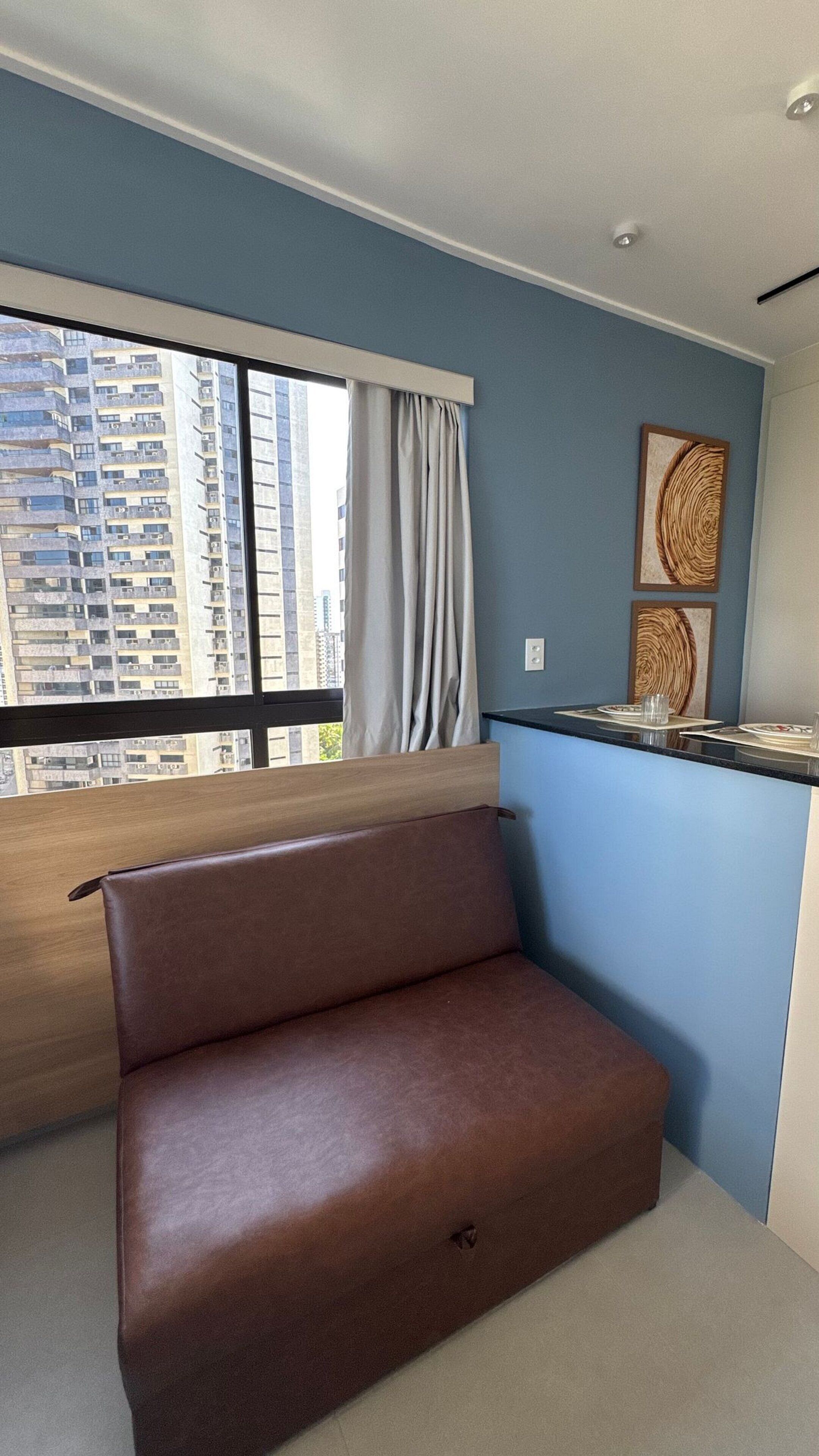 Uma sala de estar moderna com sofá, área de jantar com mesa e cadeiras, janela com cortinas e vista para edifícios altos.