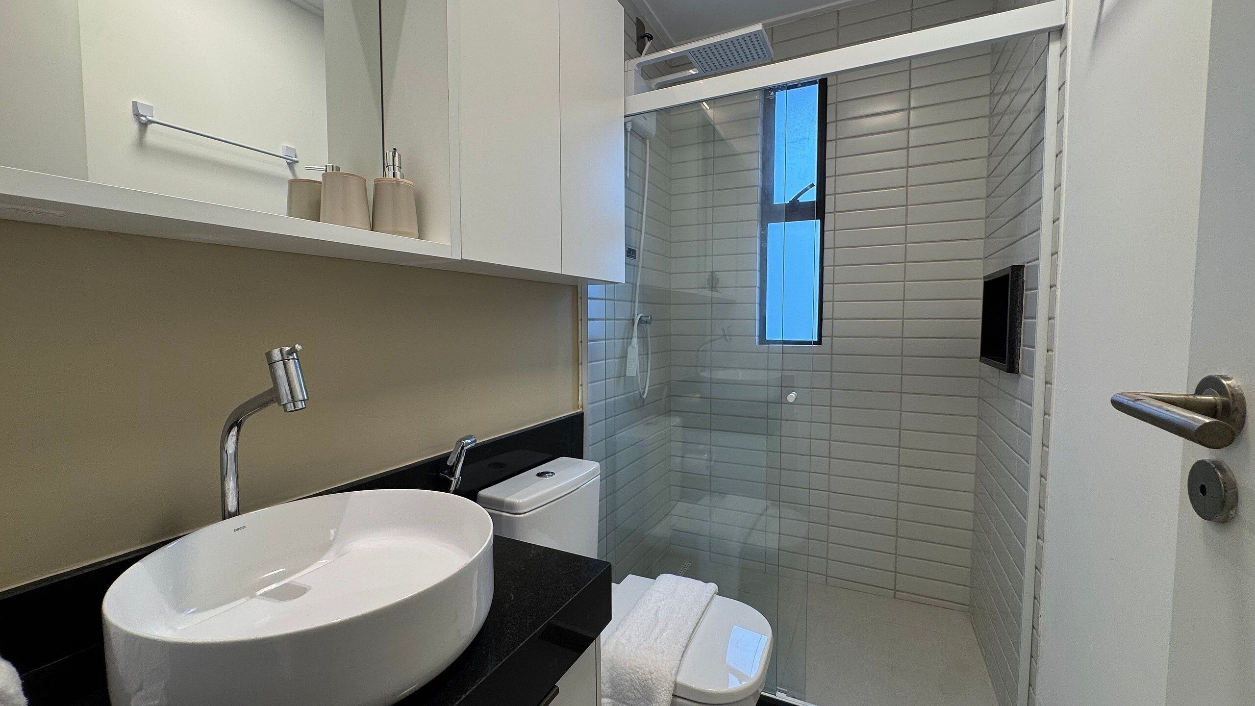 A modern bathroom with a white sink, black countertop, and a glass shower enclosure.