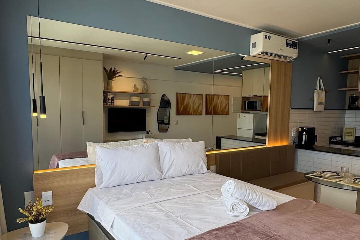 Una habitación de hotel moderna con una cama grande, una mesita redonda pequeña, un espejo, un televisor y una kitchenette.