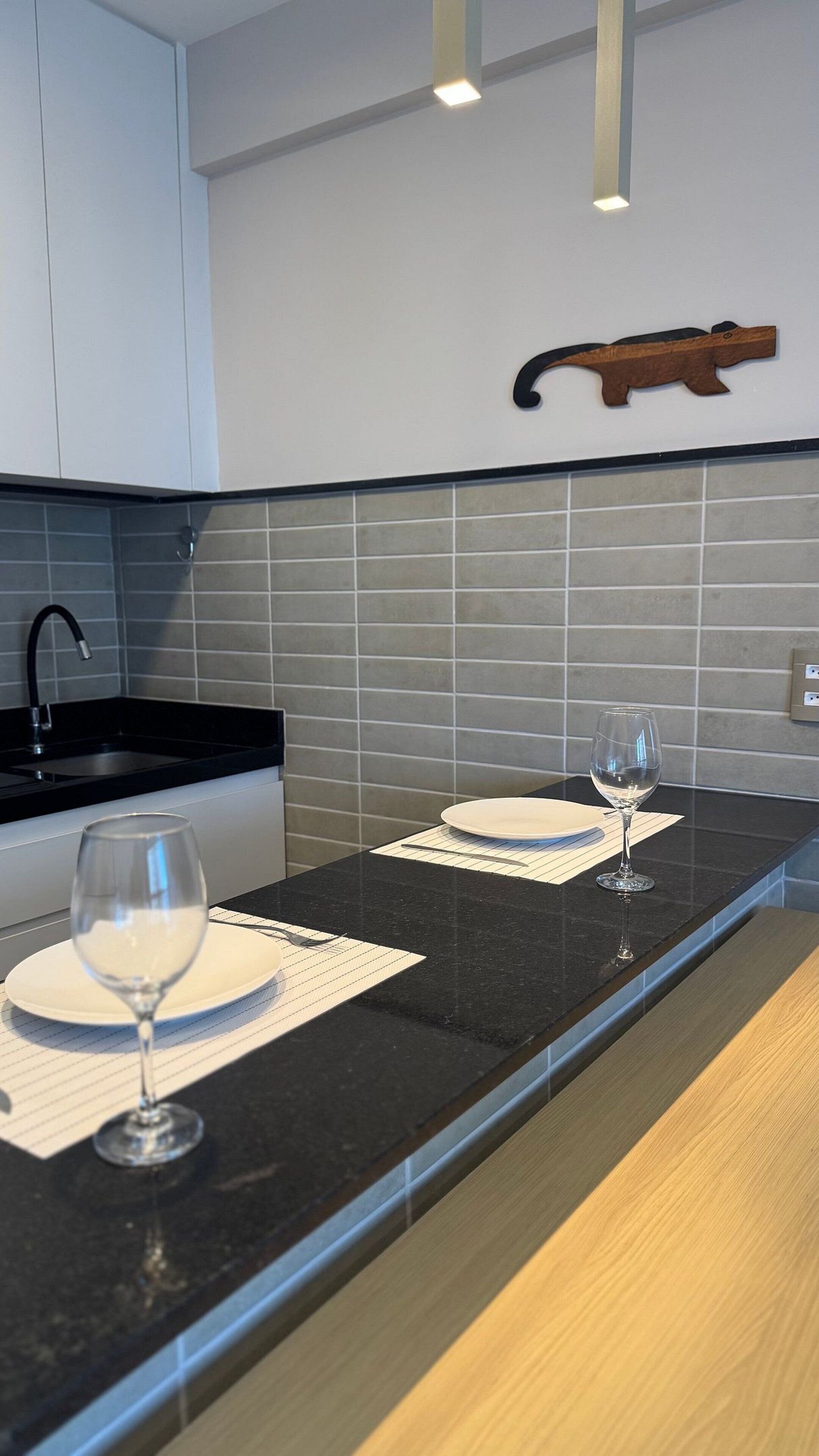 A modern kitchen with a black countertop, two wine glasses, and a knife hanging on the wall.