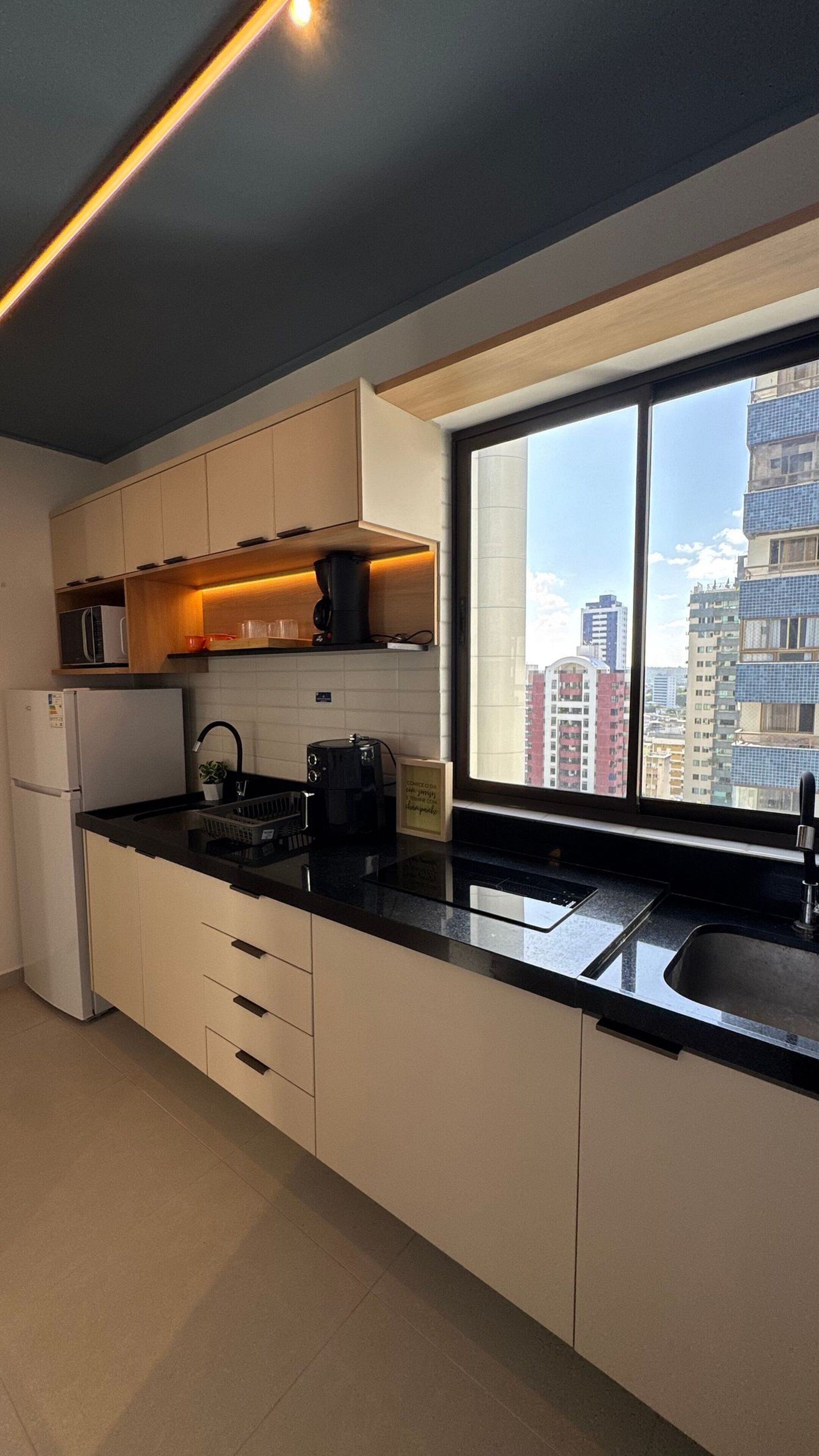 A modern kitchen with a large window, white cabinets, and a black countertop.