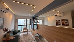 A modern living room with a sofa, armchair, coffee table, and a dining area with a wooden partition.