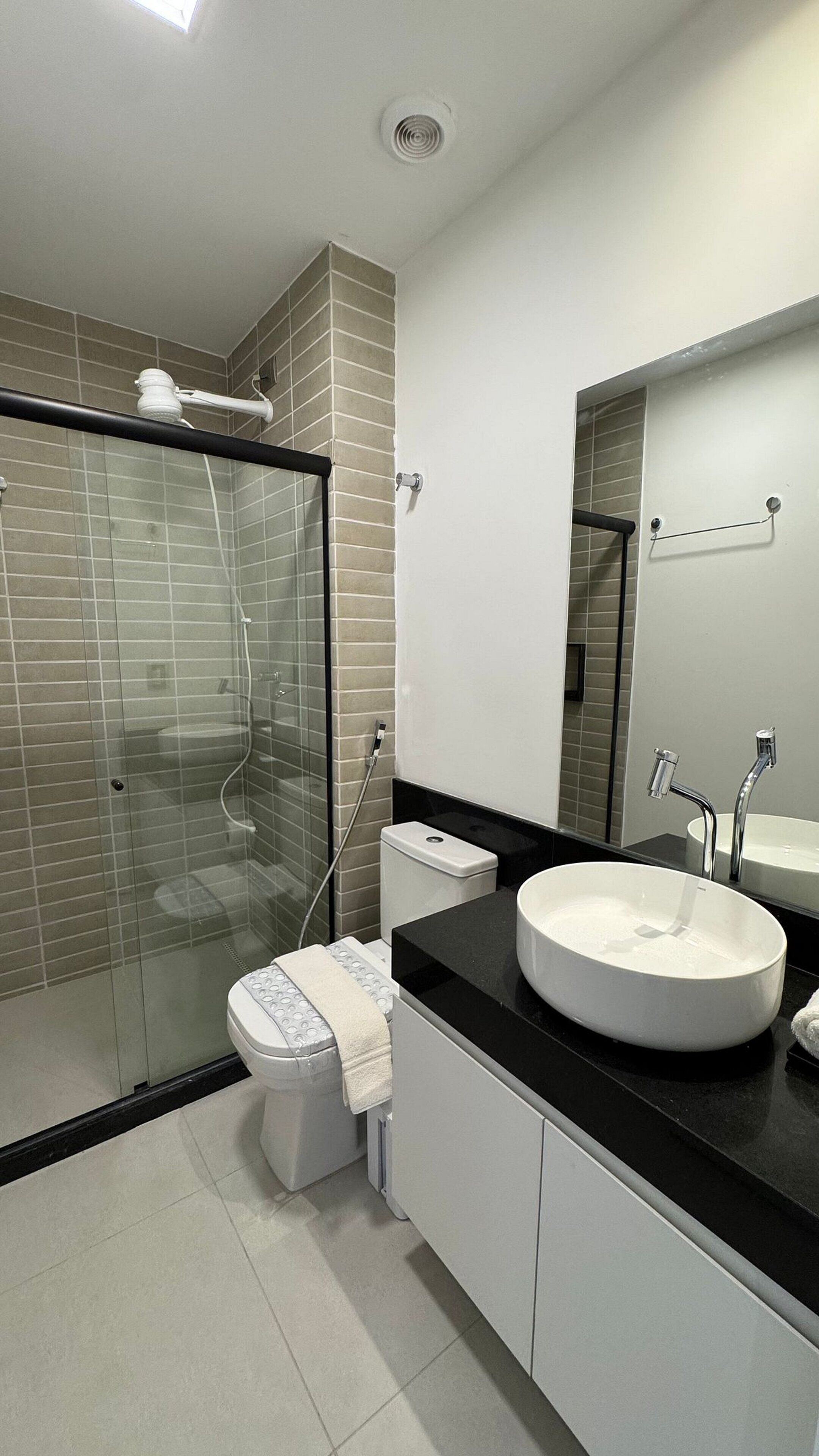 Un baño moderno con ducha de vidrio, inodoro blanco, un lavabo redondo grande y un espejo sobre el lavabo.