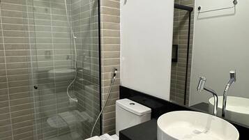 Un baño moderno con ducha de vidrio, inodoro blanco, un lavabo redondo grande y un espejo sobre el lavabo.