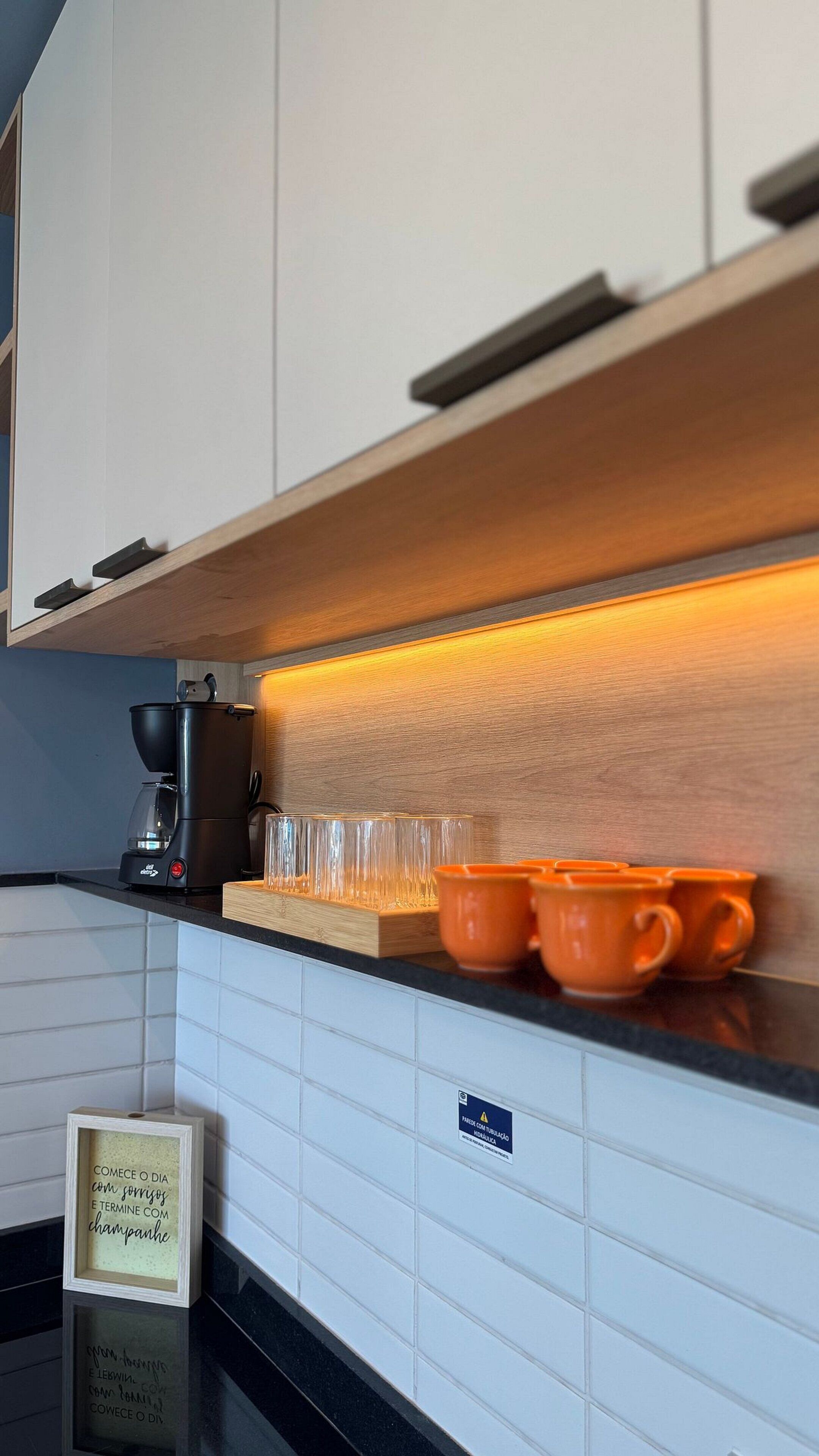 Una cocina con una cafetera, tazas naranjas y un cartel con un mensaje.