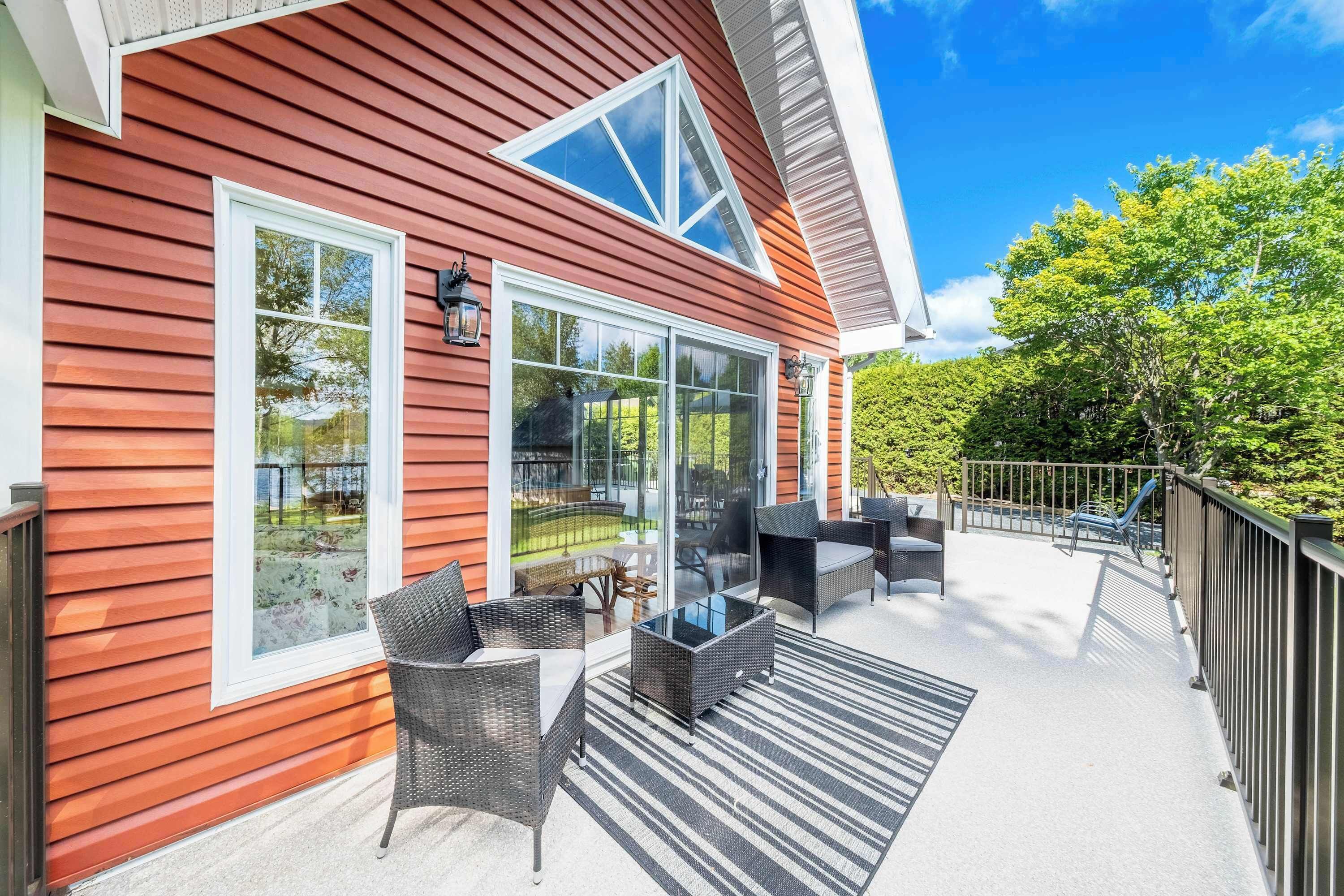 Un patio cubierto con mobiliario exterior, ventanas amplias y vista a un jardín trasero.