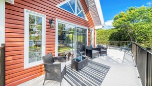 A covered patio with outdoor furniture, large windows, and a view of a backyard.