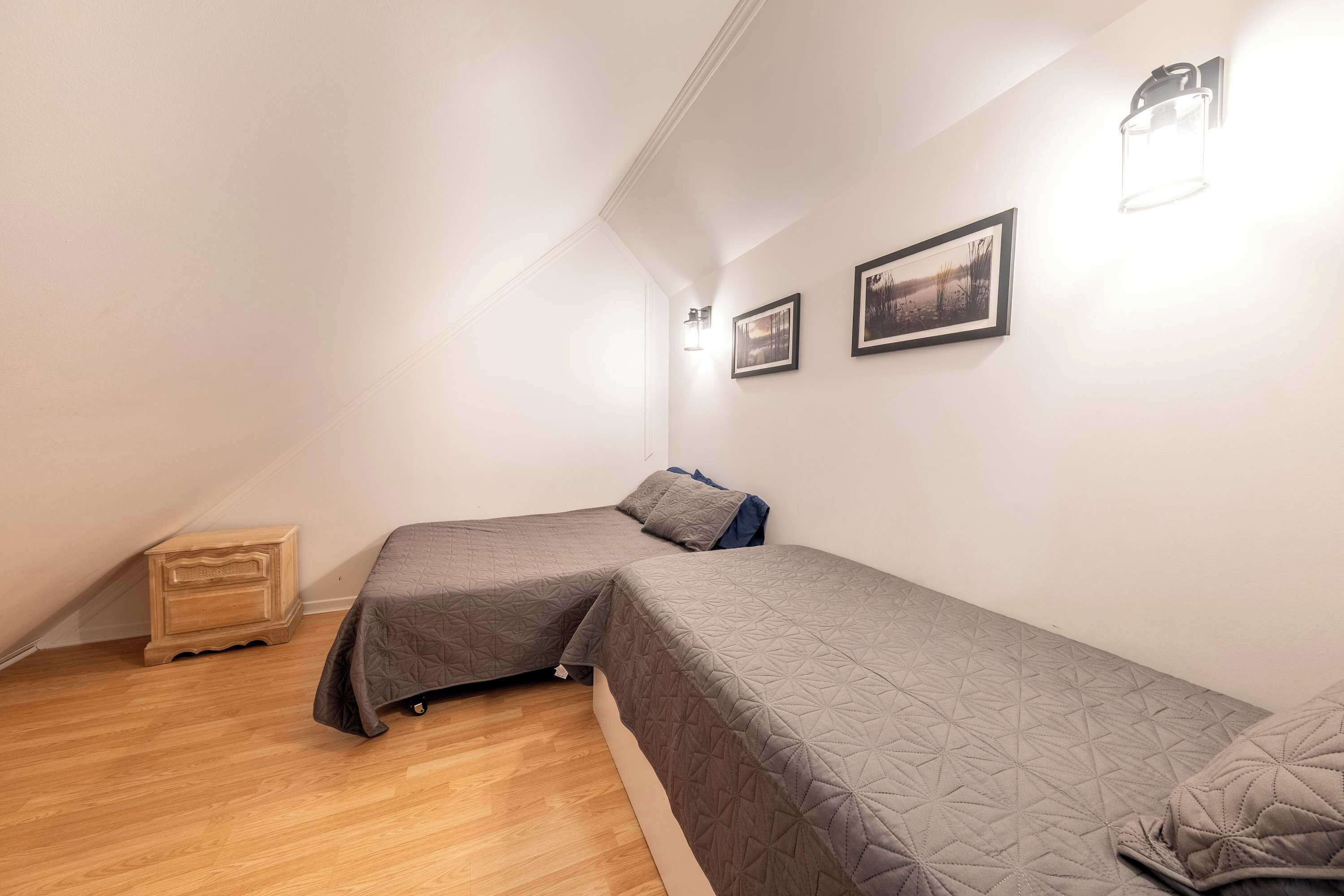 A small, well-lit room with two single beds, a wooden nightstand, and two wall-mounted light fixtures.