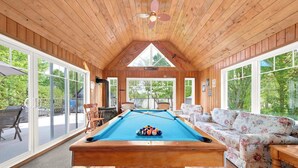 A pool table in a room with wooden walls and large windows.