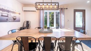 A dining area with a wooden table, metal chairs, a chandelier, and a wall-mounted air conditioner.