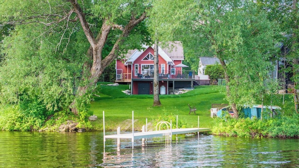 A lakeside house with a dock, surrounded by lush greenery and a clear view of the water.