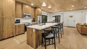 Eine moderne Küche mit Holzausbau, einer zentralen Kochinsel, Barhocker und einem Essbereich mit Blick ins Freie.