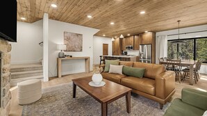 Ein modernes Wohnzimmer mit Holzbalkendecke, einem Ledersofa, einem Couchtisch und einer Küche im Hintergrund.