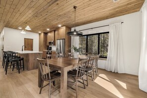 A modern kitchen with wooden cabinets, a central island, and a dining area with wooden chairs. - Legend's Lodge - Yellowstone's perfect home base / AC / Wi-Fi / Fire Pit (Island Park)