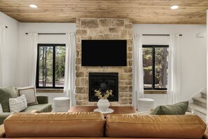 A living room with a stone fireplace, a flat-screen TV, a sofa, and a dining table. - Legend's Lodge - Yellowstone's perfect home base / AC / Wi-Fi / Fire Pit (Island Park)