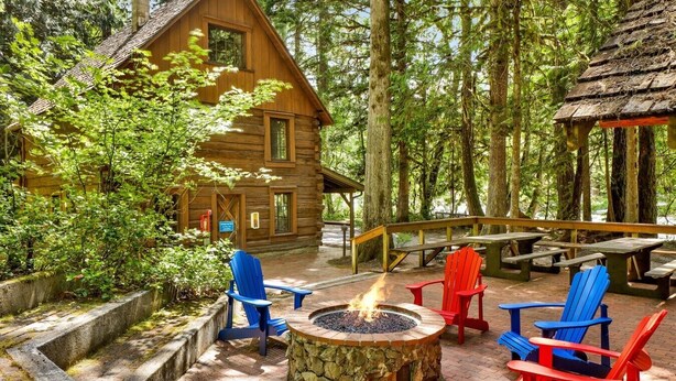 A log cabin with a stone fire pit and Adirondack chairs.