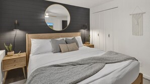 A bedroom with a bed, a round mirror, a ceiling fan, bedside lamps, a nightstand, and a macrame wall hanging.