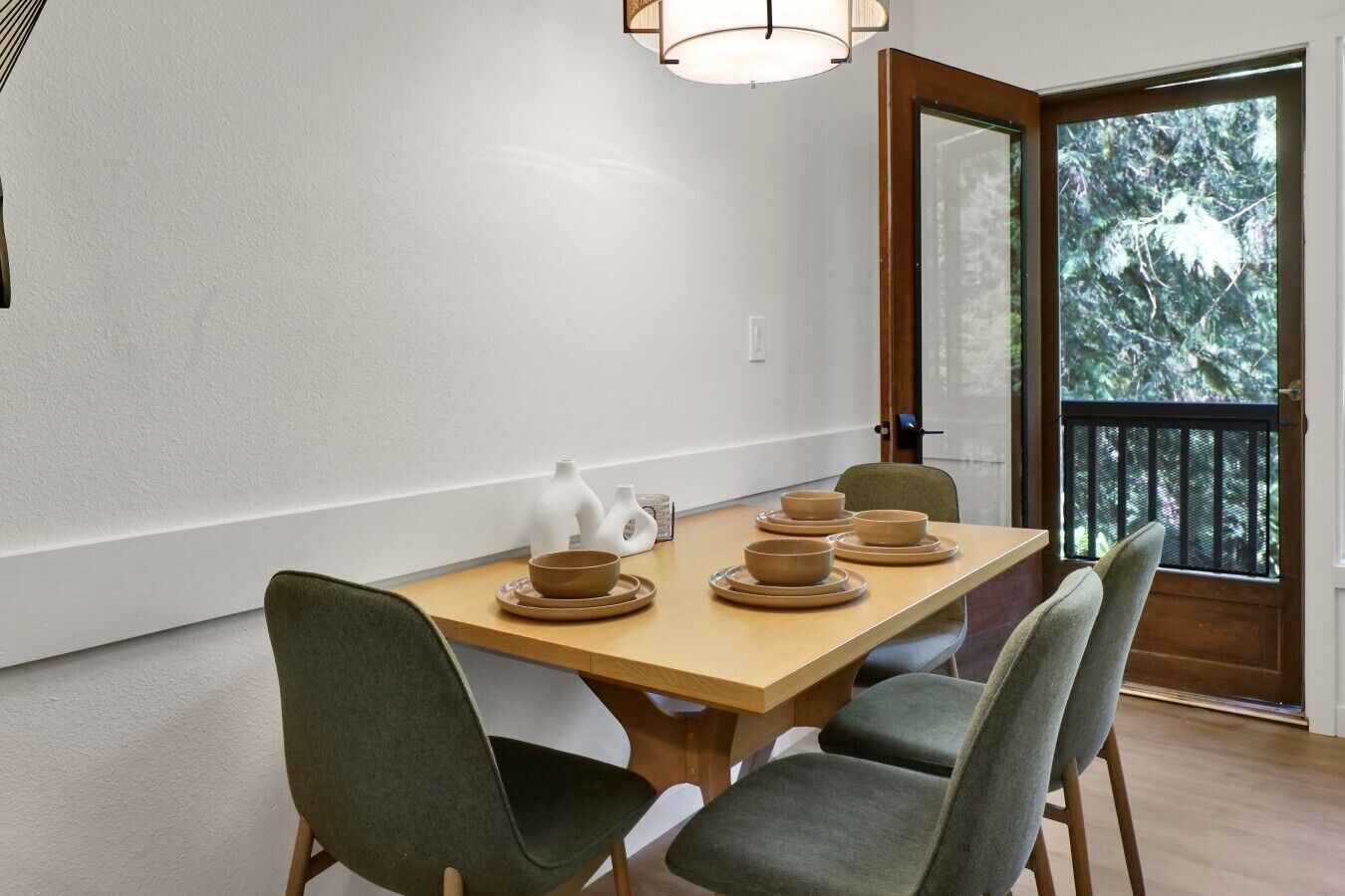 Un coin repas avec une table en bois, quatre chaises et une vue sur les arbres, visible à travers une porte.