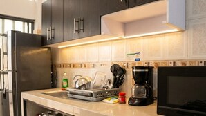 Una cocina con armarios oscuros, un refrigerador de acero inoxidable, una cafetera y un microondas.