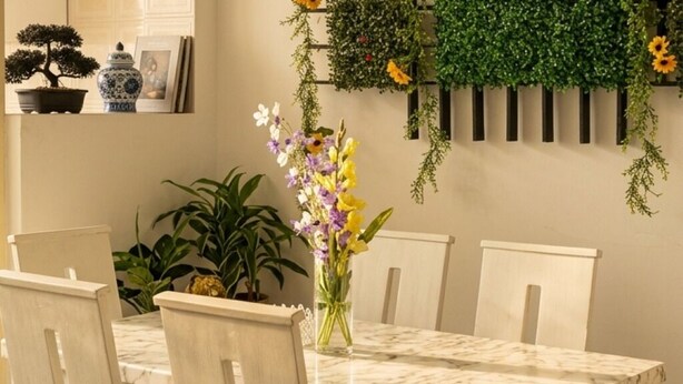 Una mesa de comedor con sillas, un jarrón con flores y plantas en macetas.