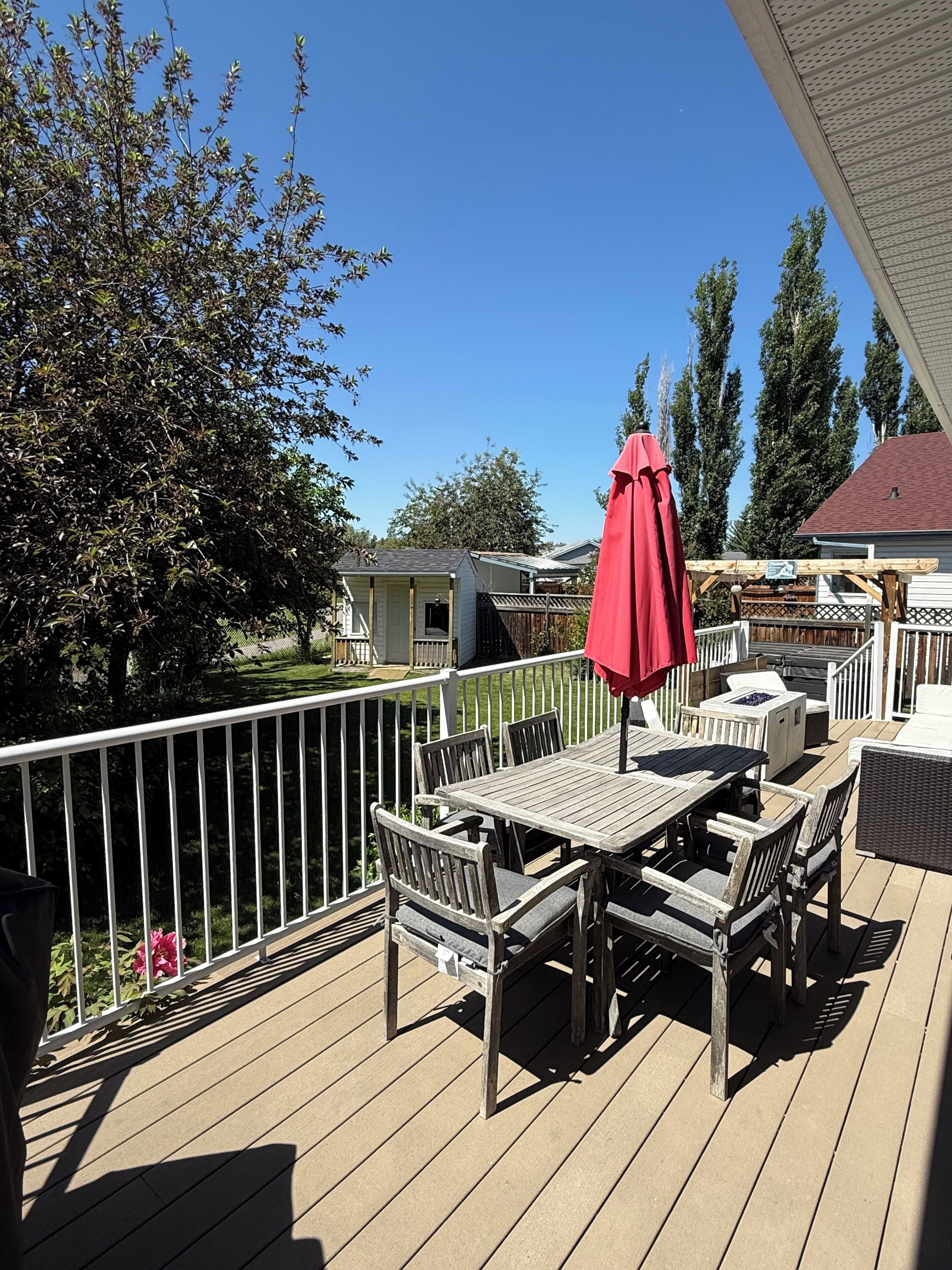 Une terrasse en bois avec une table et des chaises, un parasol rouge et une balustrade blanche.