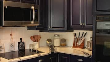 Une cuisine dotée de meubles de rangement aux couleurs sombres, d’un four à micro-ondes, d’un réfrigérateur et d’un plan de travail sur lequel sont posés des ustensiles de cuisine.