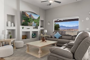 A living room with a sofa, a coffee table, a TV, and a window with a mountain view. - Mountain Vista Hideaway by J and Amy BL 992768 (Mesquite)