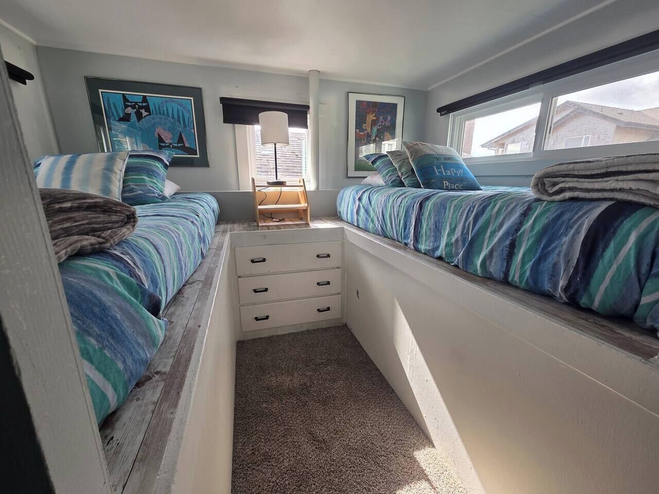 A compact bedroom with two beds, a small storage unit, and artwork on the walls.