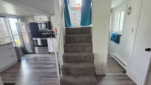 A staircase leading to a second floor, a kitchen area with appliances, and a hallway with a door. - Arch Cape cottage with a View (Arch Cape)