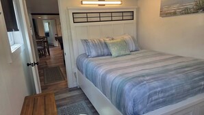 A bedroom with a bed, bedside tables, a headboard with a light fixture, and a painting on the wall. - Arch Cape cottage with a View (Arch Cape)