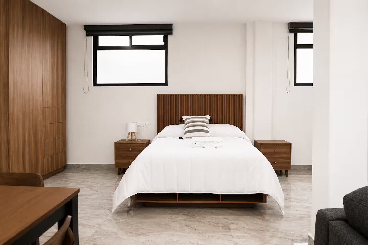 Een moderne slaapkamer met een houten hoofdbord, een witte spreidekking, twee nachtkastjes en een houten garderobe.