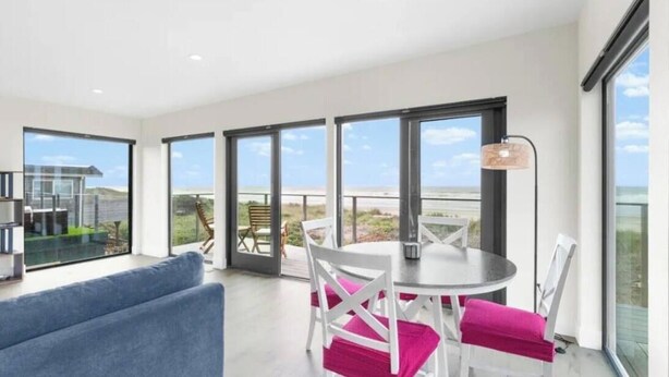 A modern room with a balcony, large windows, a round table with chairs, and a blue sofa. - New Modern Oceanfront W/ Panoramic Ocean Views (Rockaway Beach)