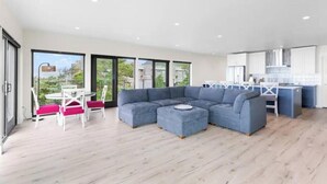 A modern living room with a sectional sofa, a dining table with chairs, and a kitchen area. - New Modern Oceanfront W/ Panoramic Ocean Views (Rockaway Beach)