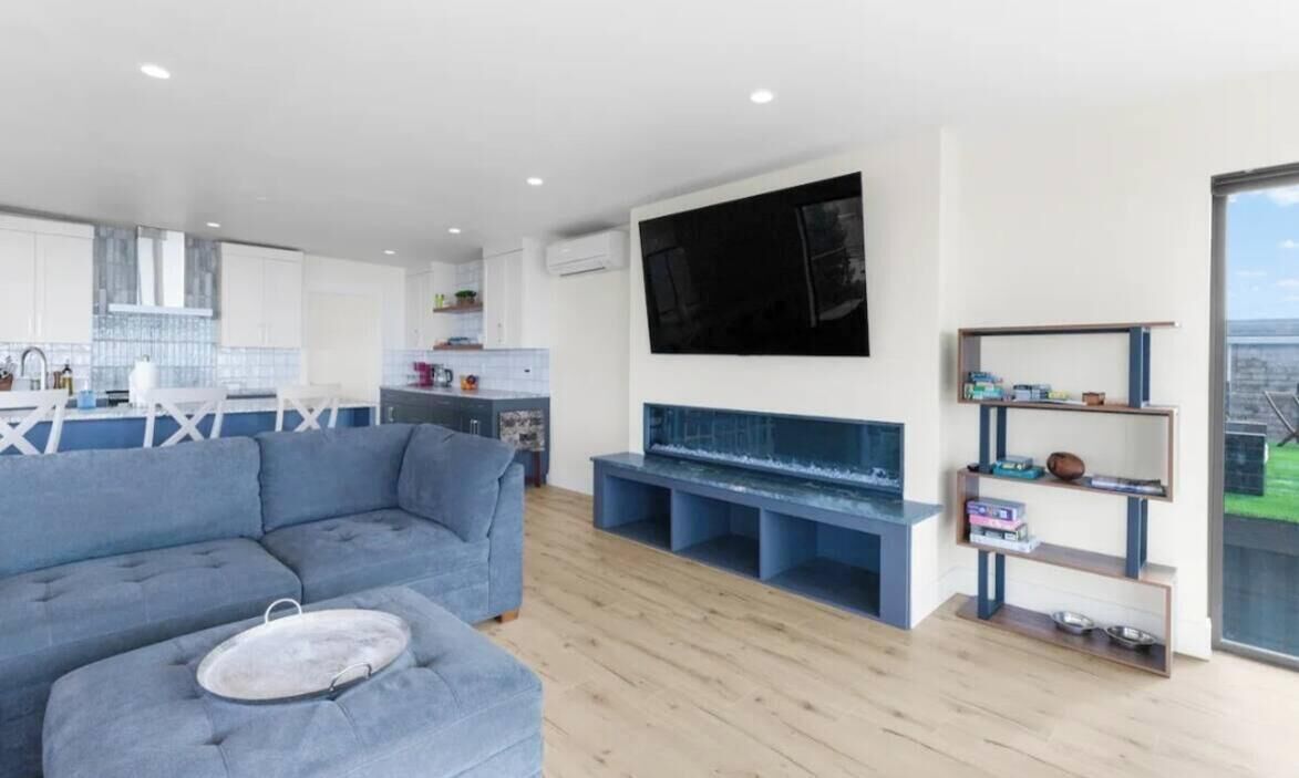 Ein modernes Wohnzimmer mit einer Eckcouch, einem Flachbildfernseher an der Wand und Holzboden.
