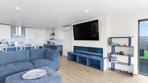 A modern living room with a sectional sofa, a flat-screen TV mounted on the wall, and a wooden floor. - New Modern Oceanfront W/ Panoramic Ocean Views (Rockaway Beach)