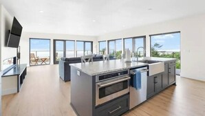 A modern kitchen with a large island, built-in oven, and a flat-screen TV. - New Modern Oceanfront W/ Panoramic Ocean Views (Rockaway Beach)