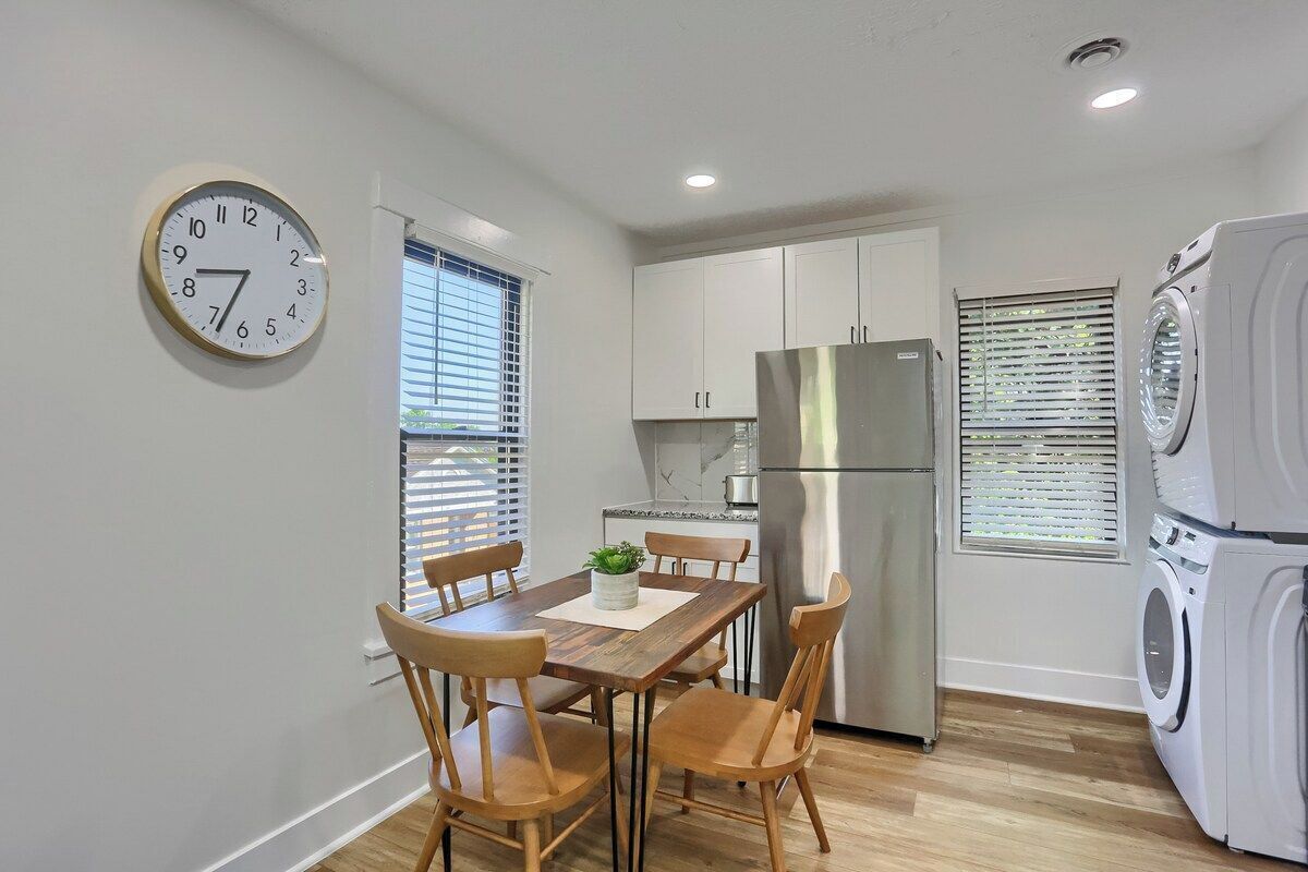 A compact kitchen with a dining table, chairs, a clock, a refrigerator, and a washing machine.