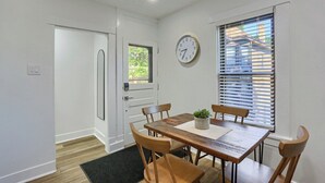 A dining area with a wooden table, four chairs, a potted plant, a wall clock, and a window with blinds. - Dormont, Potomac @3 Stylish and Cozy 2 Bedroom Private Apartment (Pittsburgh)