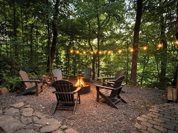 An outdoor seating area with Adirondack chairs and a fire pit surrounded by trees.