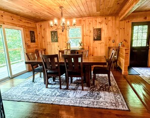 A wooden dining room with a chandelier, a table, chairs, and a rug.