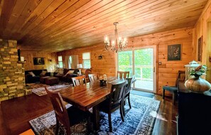 Interior de una cabaña de madera con comedor, sala de estar y un amplio ventanal.