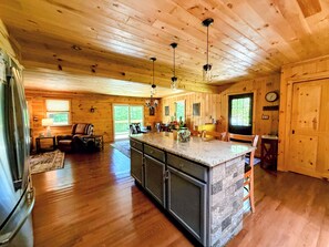 A spacious kitchen with a large island, wooden walls, and a stone backsplash.