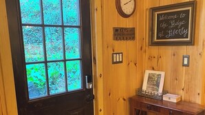 A wooden door with a window, a wall clock, a welcome sign, a small table with a framed picture, and a fire extinguisher. - Modern 4-bedroom cabin close to Liberty Mountain (Fairfield)